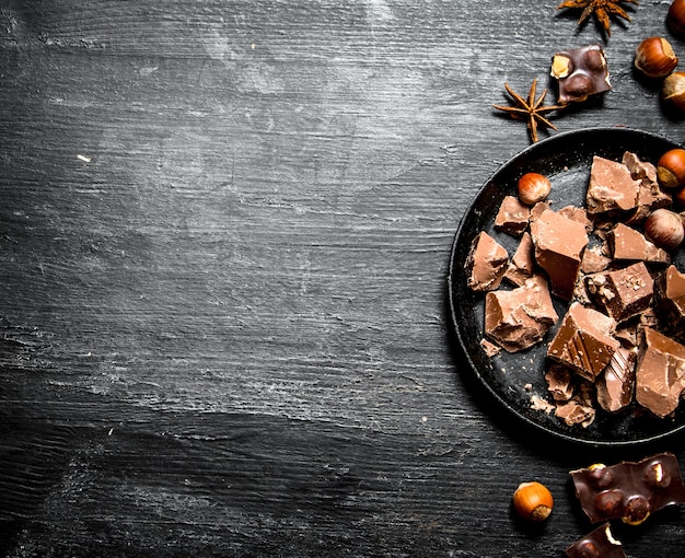 Morceaux de chocolat avec des noix entières. Sur un fond en bois noir.