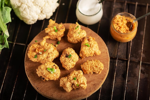 Morceaux de chou-fleur frit avec des sauces végétaliennes sur une assiette sur un fond sombre Ailes de chou-fleur alimentaire