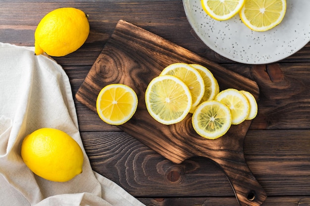 Des morceaux de citron ronds tranchés sur une planche à découper et des citrons entiers sur une table en bois. Nutrition biologique, source de vitamines. Vue de dessus