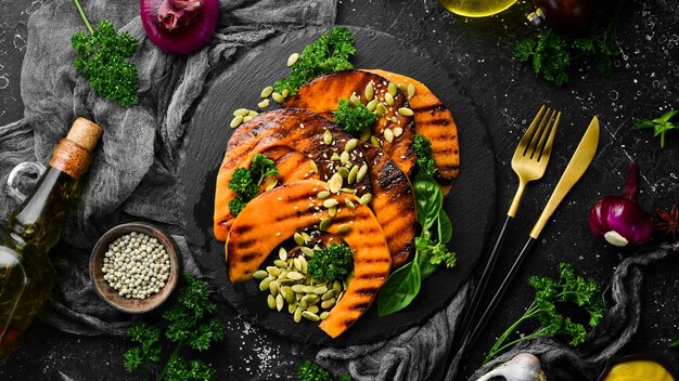 Morceaux de citrouille cuits au four avec des graines de citrouille dans une assiette en pierre noire Menu d'automne Régime Vue de dessus Espace libre pour le texte