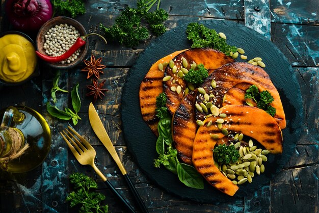 Morceaux de citrouille cuits au four avec des graines de citrouille dans une assiette en pierre noire Menu d'automne Régime Vue de dessus Espace libre pour le texte