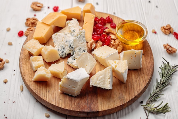 Morceaux de divers fromages aux noix et au miel sur un fond en bois blanc