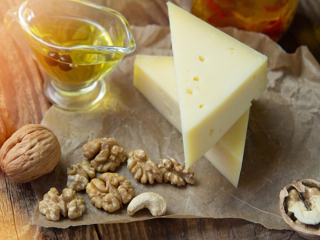 Morceaux de fromage sur papier parchemin avec noix et huile d'olive sur une vieille table en bois