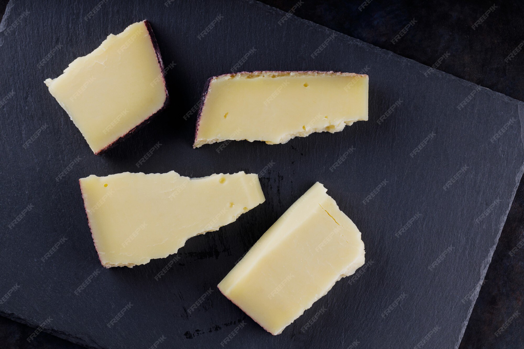 Morceaux de fromage à pâte dure sur fond sombre. Fromage de chèvre sur une ardoise. Fromage
