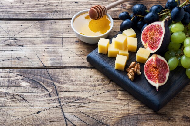 Morceaux de fromage, raisins de figues de fruits frais, miel et noix sur une planche à découper en bois. fond