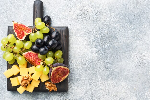 Morceaux de fromage, raisins de figues de fruits frais, miel et noix sur une planche à découper en bois. fond