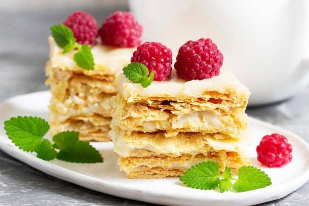 Morceaux de gâteau Napoléon décorés de framboises et de feuilles de mélisse sur fond clair.