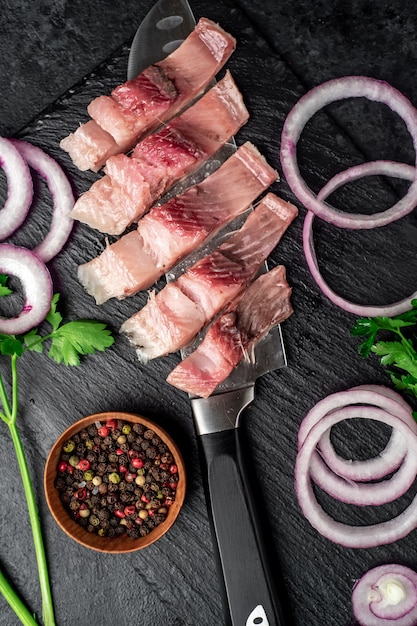 Morceaux de hareng mariné sur un couteau avec des oignons et des herbes sur une table en pierre