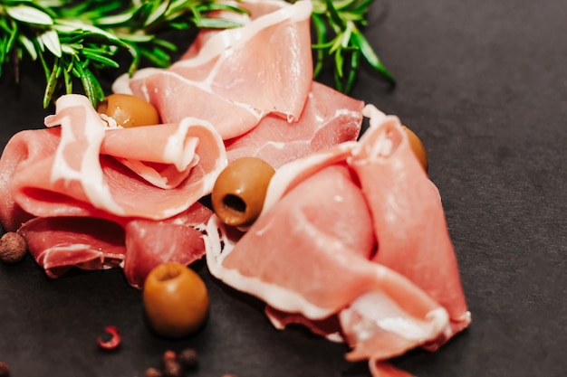 Des morceaux de jambon de porc séché avec des olives sur une planche noire