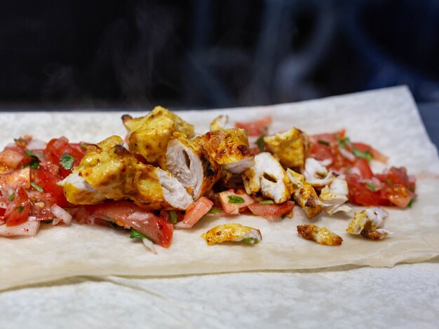 Des morceaux juteux de brochette de poulet se trouvent sur du pain pita mince avec des légumes hachés