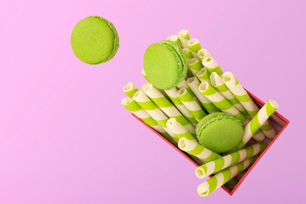 Morceaux de macarons à la pistache verte ou macarons français tombant sur une boîte cadeau rouge