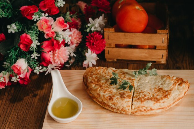 Morceaux d'omelette sur un bureau de cuisine en bois avec de l'huile, des tomates et un bouquet de fleurs sur les côtés