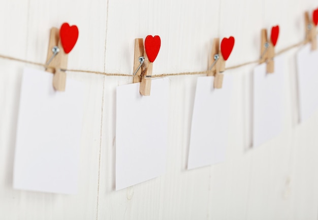 Morceaux de papier blancs sur des pinces à linge avec un coeur sur un fond en bois