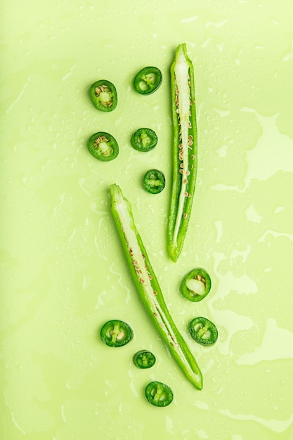 Morceaux de piments verts allongés sur un fond de couleur avec des gouttes d'eau Vue de dessus mise à plat