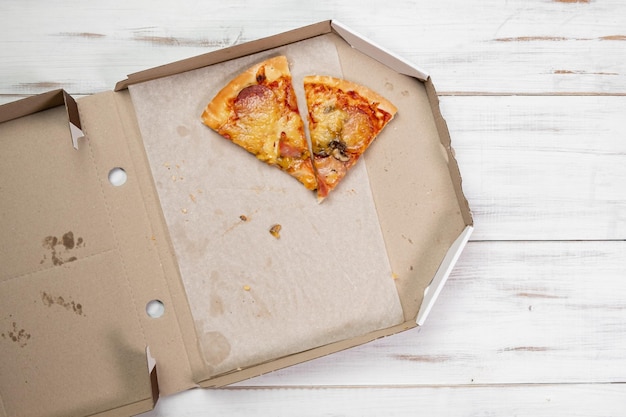 Morceaux de pizza dans une boîte en carton fond de bois blanc Concept alimentaire Vue de dessus