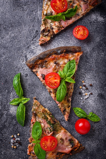 Morceaux de pizza noire aux tomates et au basilic