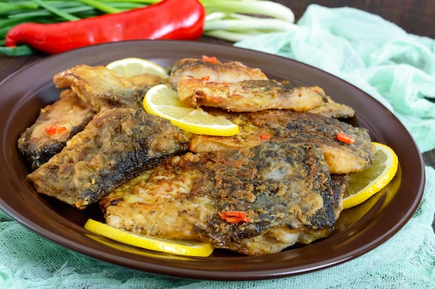 Morceaux de poisson frit (carpe) sur une plaque en céramique sur un fond en bois foncé.