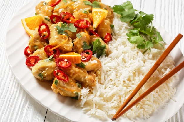 Morceaux de poitrine de poulet épicés glacés à la mangue avec du riz sur une assiette blanche avec des baguettes sur une table en bois vue horizontale d'en haut