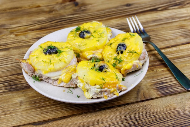 Morceaux de porc au four avec fromage à l'ananas et olive sur une table en bois