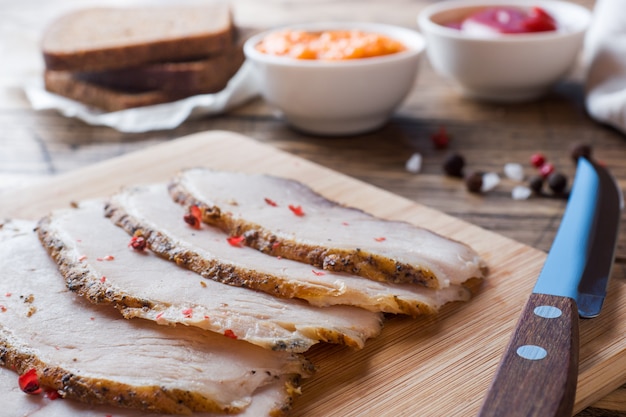 Morceaux de porc bouilli fumé sur une planche en bois rustique avec du pain, des sauces et des épices sur une table en bois