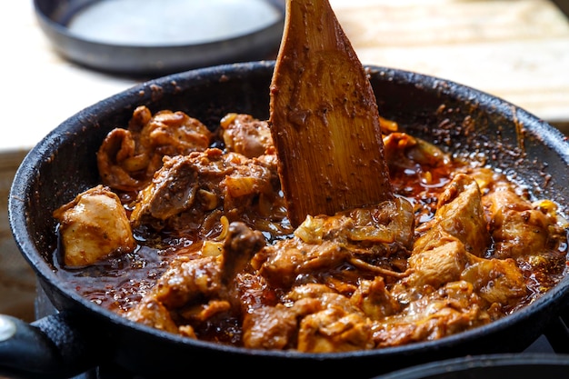 Morceaux de poulet cuits en sauce aux épices dans une poêle profonde avec une spatule en bois