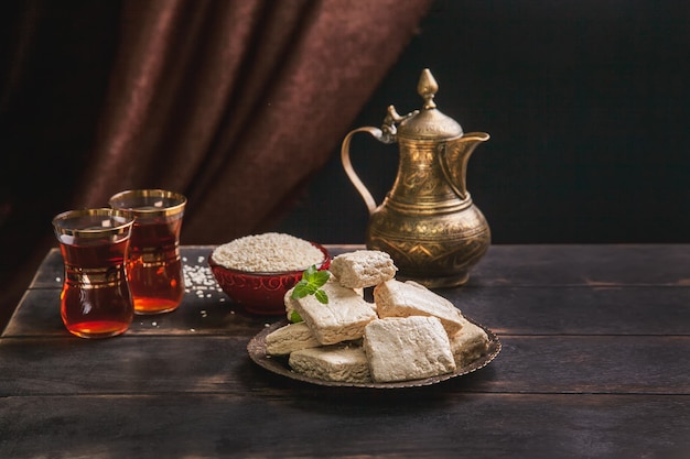 morceaux de tahini halva, graines de sésame dans un bol, thé dans des armudas turcs une cruche vintage