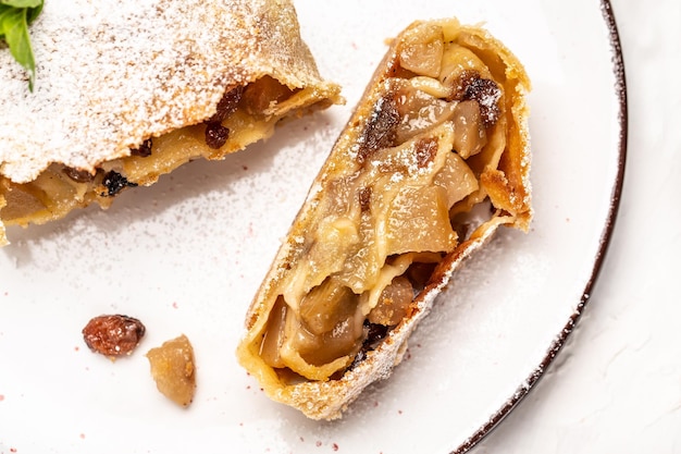 Morceaux traditionnels de strudel aux pommes avec du sucre en poudre à la cannelle et aux raisins secs sur fond clair Vue de dessus Arrière-plan de recette alimentaire Gros plan