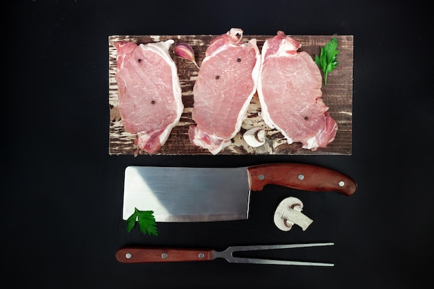 Morceaux de viande de rôti de bœuf crue pour griller sur une planche à découper de cuisine avec un couteau à l'ail et aux champignons persil et une fourchette à viande