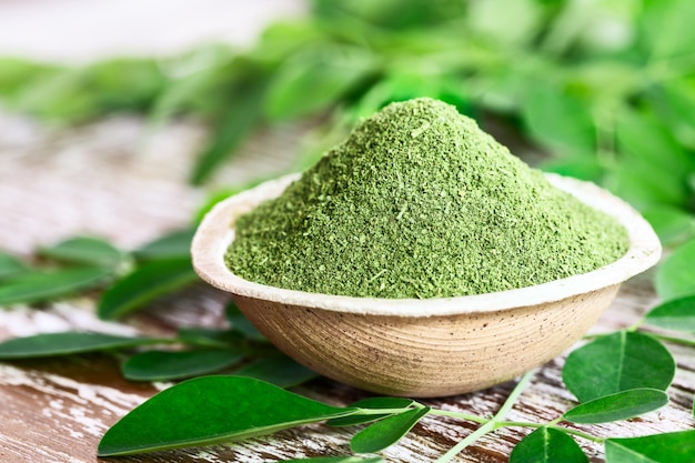 Moringa en poudre dans un bol avec des feuilles de Moringa fraîches