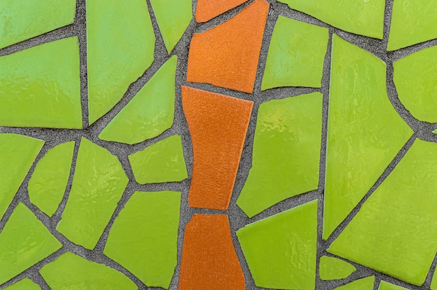 Mosaïque brillante de carreaux de céramique verts et orange cassés sur le mur.