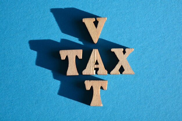 Photo le mot et l'acronyme de la tva en lettres d'alphabet en bois sous forme de mots croisés isolés sur fond bleu avec espace de copie