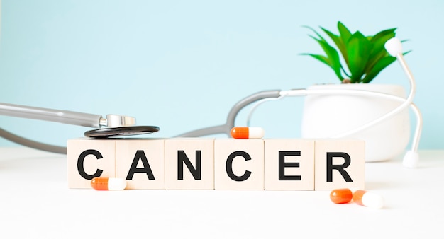 Le mot CANCER est écrit sur des cubes en bois près d'un stéthoscope sur un fond en bois. Concept médical
