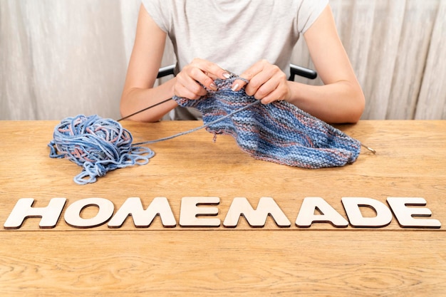 mot fait maison est disposé en lettres de bois sur une vieille table en bois où une femme tricote