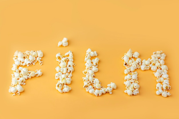 Le mot "film" est disposé à partir de pop-corn frais sur fond orange. Concept de collation de cinéma. La nourriture pour regarder un film et se divertir. Vue de dessus, pose à plat.