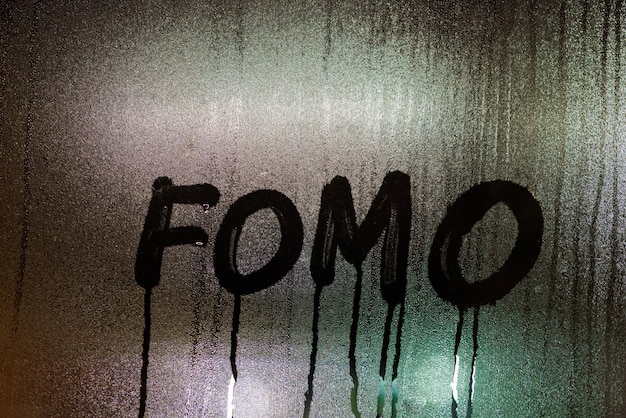 Mot FOMO Fear Of Missing Out écrit à la main sur la surface de la vitre humide de la nuit