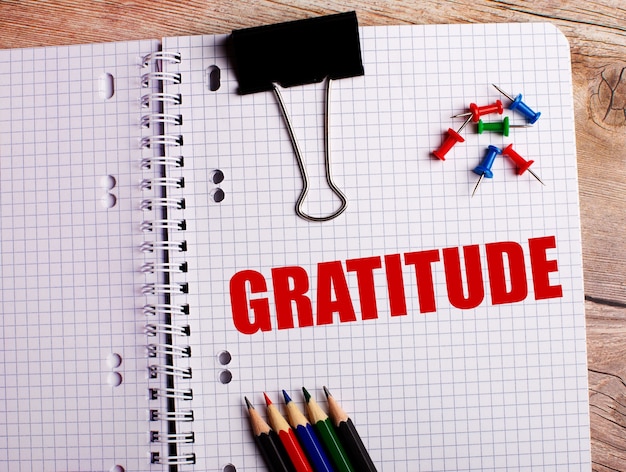 Le mot GRATITUDE est écrit dans un cahier près de crayons multicolores et de boutons sur un mur en bois.