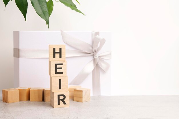 Mot HÉRITIER composé de blocs de construction sur la table à côté d'une fleur et d'une boîte cadeau