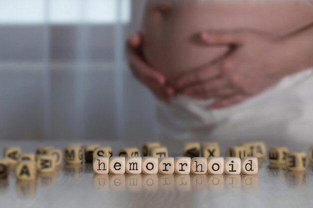 Mot HEMORRHOID composé de lettres en bois. Femme enceinte en arrière-plan