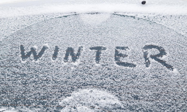 Mot hiver écrit à la main sur la fenêtre de la voiture enneigée à la lumière du matin d'hiver