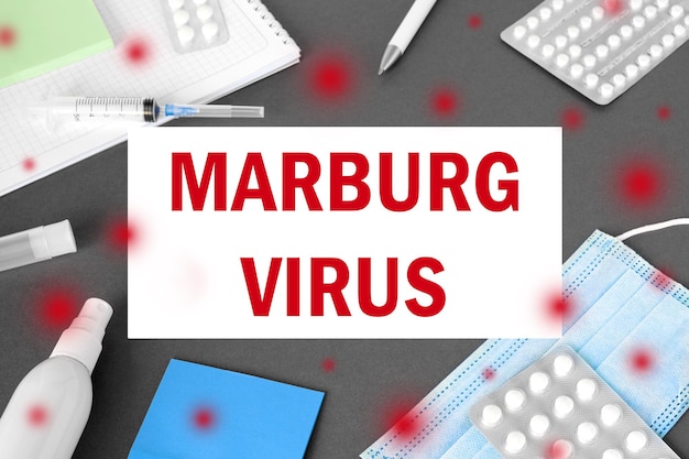 Le mot Marburgvirus sur fond de table de bureau de médecin moderne gris Masque bloc-notes seringue désinfectant et fournitures MARV Marburg Virus propagation Médecine et soins de santé éducation médicale Vue de dessus