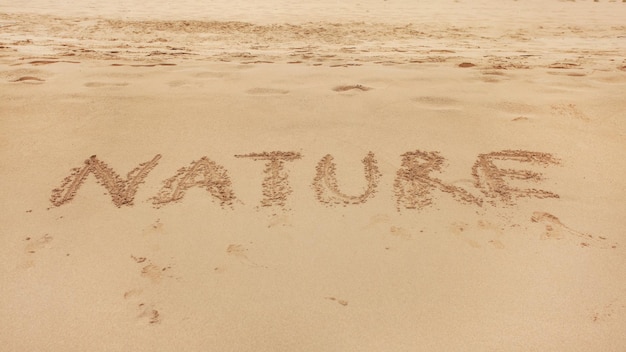 Mot NATURE écrit à la main dans le sable humide de la plage.