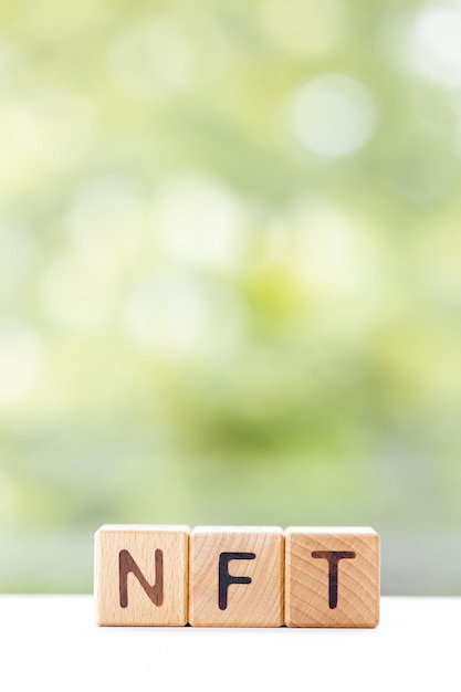 Le mot NFT est écrit sur des cubes en bois sur un fond d'été vert Gros plan d'éléments en bois