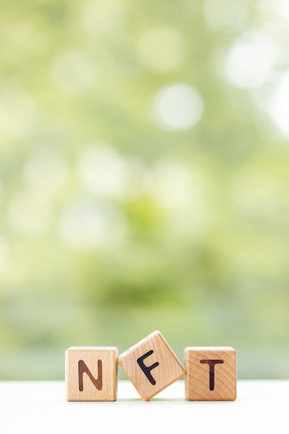 Le mot NFT est écrit sur des cubes en bois sur un fond d'été vert Gros plan d'éléments en bois