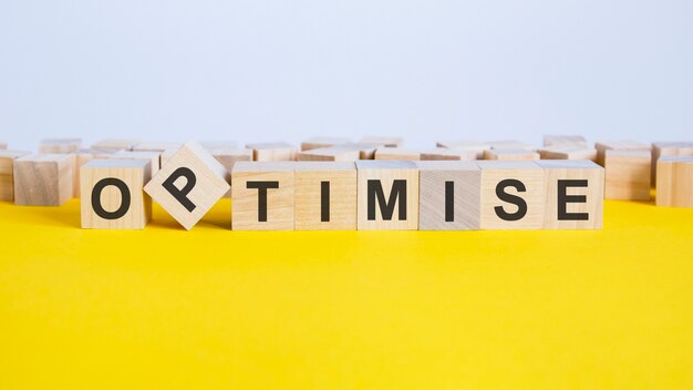 Le mot optimiser est composé de cubes en bois posés sur une table jaune. l'un des cubes est placé sur un bord, fond gris, concept d'entreprise