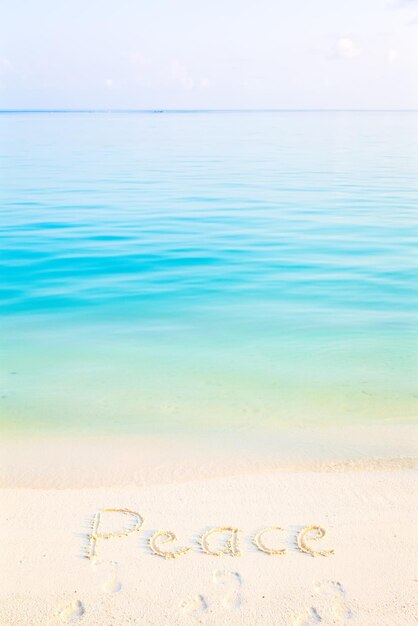 Photo le mot paix écrit dans le sable sur une plage avec le fond de la mer du matin