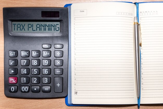 Mot de planification fiscale sur la calculatrice. Temps de payer l'impôt dans l'année. Calculatrice, bloc-notes et stylo sur une table en bois. Concept commercial et fiscal.