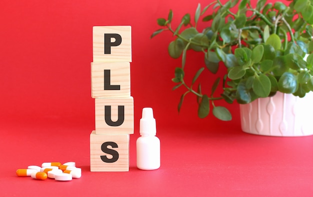 Le mot PLUS est fait de cubes en bois sur une table rouge avec des médicaments. Concept médical.