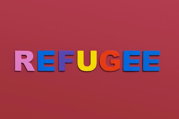 Mot de réfugiés écrit en lettres de l'alphabet en bois coloré sur fond rouge Migration sûre pour les personnes fuyant le concept de soutien et d'assistance de guerre Vue de dessus Espace de copie