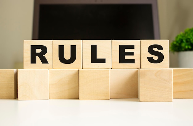 Le mot RÈGLES est écrit sur des cubes en bois posés sur la table de bureau devant un ordinateur portable