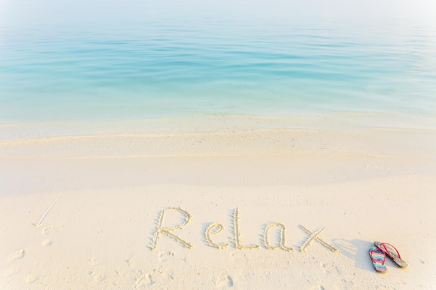 Photo le mot relax écrit dans le sable sur une plage avec le fond de la mer du matin